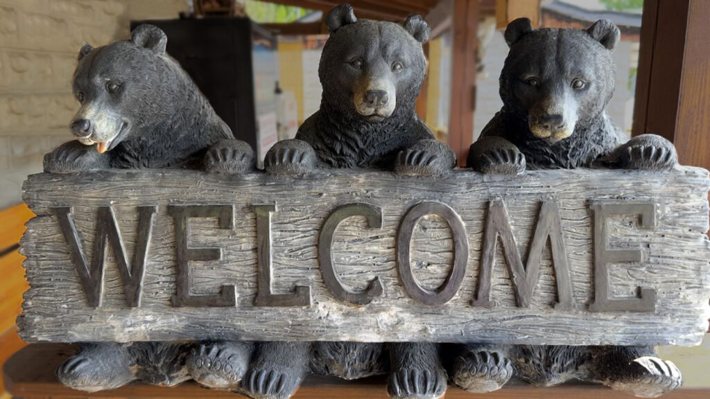three wooden bears holding a sign that says welcome