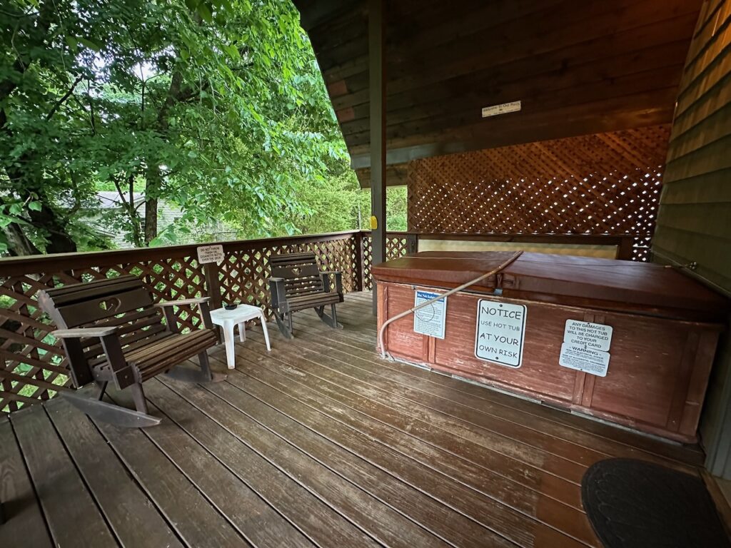 porch of cabin 20 showing hot tub with closed lid, chairs, and small table