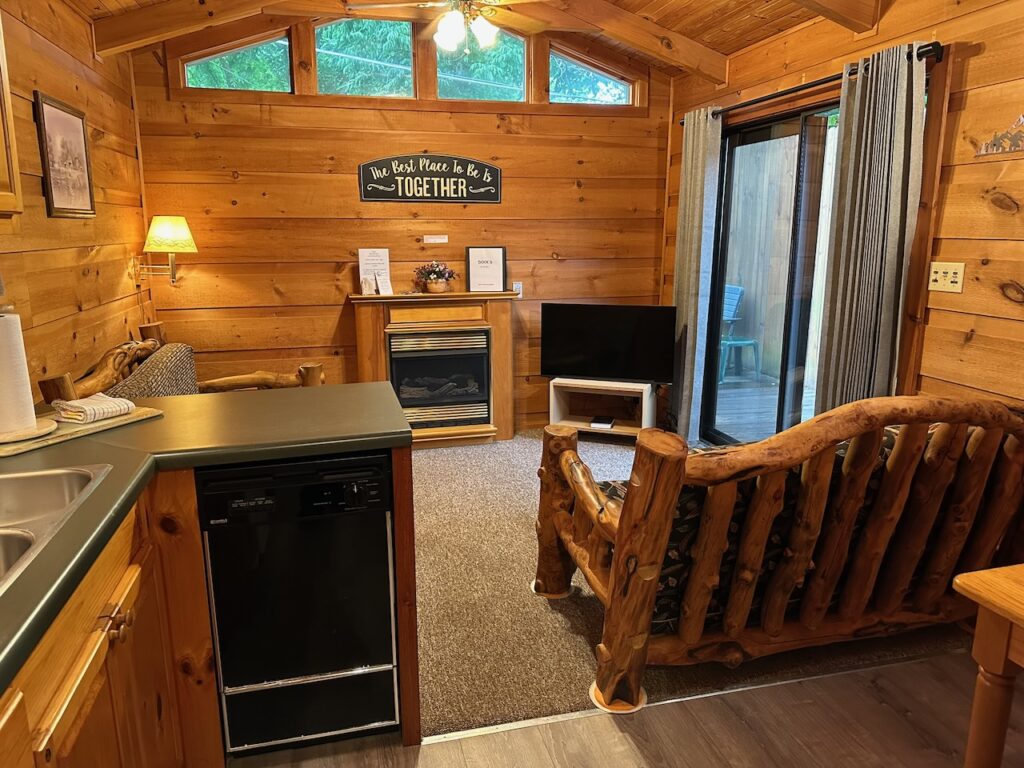 Living spaae of cabin Rendevous 2 with fireplace, log couch, sliging glass doors to deck